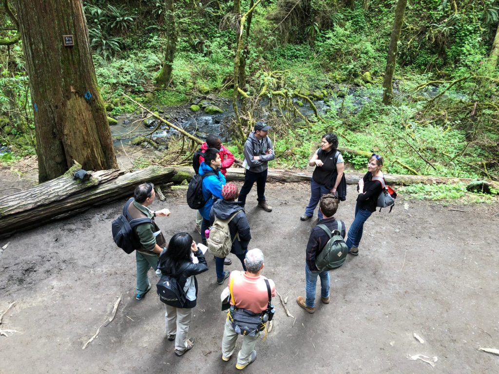 International fellows gathered on a trail near a river and green foliage