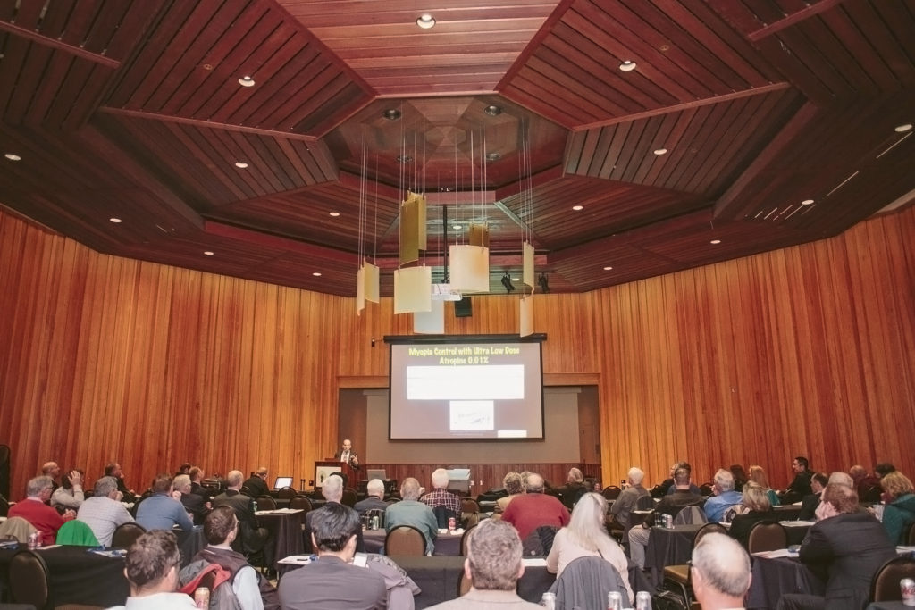 Event space filled with people watching a speaker and visual presentation