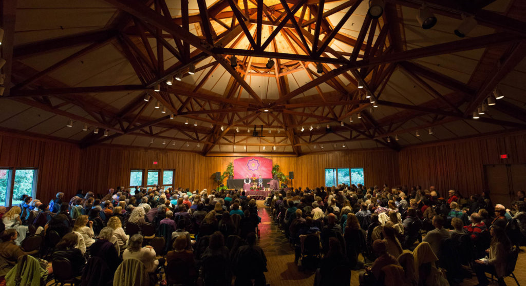 Elaborate wooden room filled with a large group of people watching a presentation